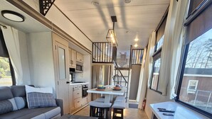 A compact RV interior with a kitchenette, a dining area, and a seating area with a sofa and ottoman. - Fenced dog yard, creek fishing access, privacy and stunning sunset views! (Schoharie)