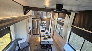 A compact RV interior with a dining area, kitchenette, and seating area with a view. - Fenced dog yard, creek fishing access, privacy and stunning sunset views! (Schoharie)
