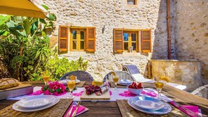 An outdoor dining area with stone walls, wicker furniture, and a table set for a meal. - Cozy home in Llubi with private swimming pool, can be inside or outside (Llubi)