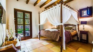 A four-poster canopy bed with a view of a stone wall and greenery outside. - Cozy home in Llubi with private swimming pool, can be inside or outside (Llubi)