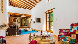 A spacious living area with a high ceiling, wooden beams, a fireplace, a television, and a colorful chair. - Cozy home in Llubi with private swimming pool, can be inside or outside (Llubi)