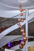 Un interior de varios niveles con una escalera espiral y lámparas colgantes esféricas de cobre.
