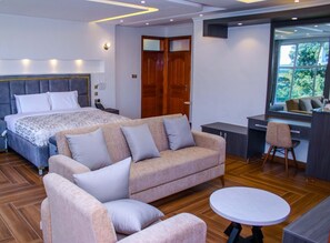 A modern bedroom with a large bed, a sofa, a desk, and a chair. - Highlands view boutique villas & resort  (Mweiga)