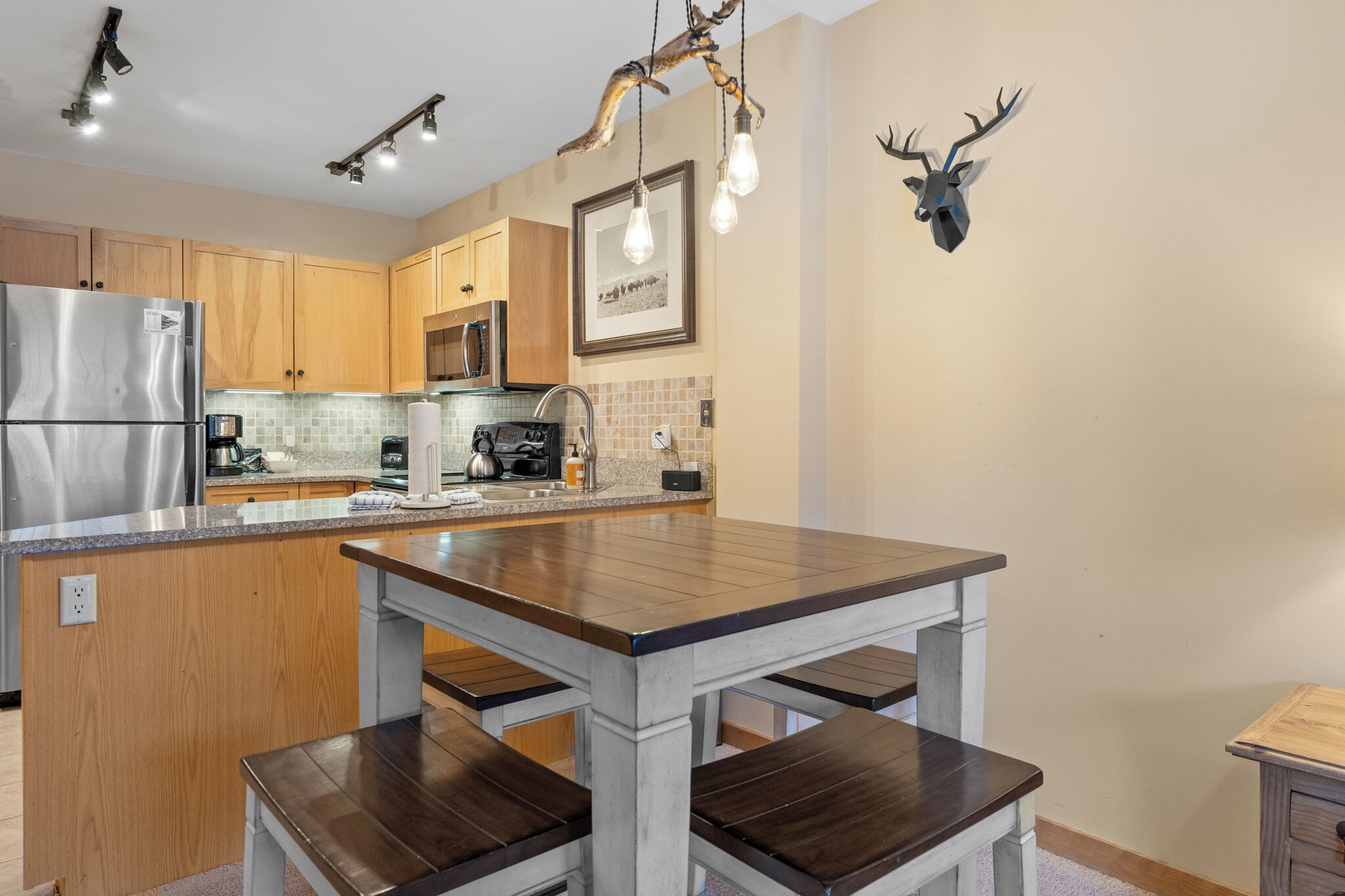 A modern kitchen with wooden cabinets, a stainless steel refrigerator, a built-in oven, and a large island with a dark countertop.
