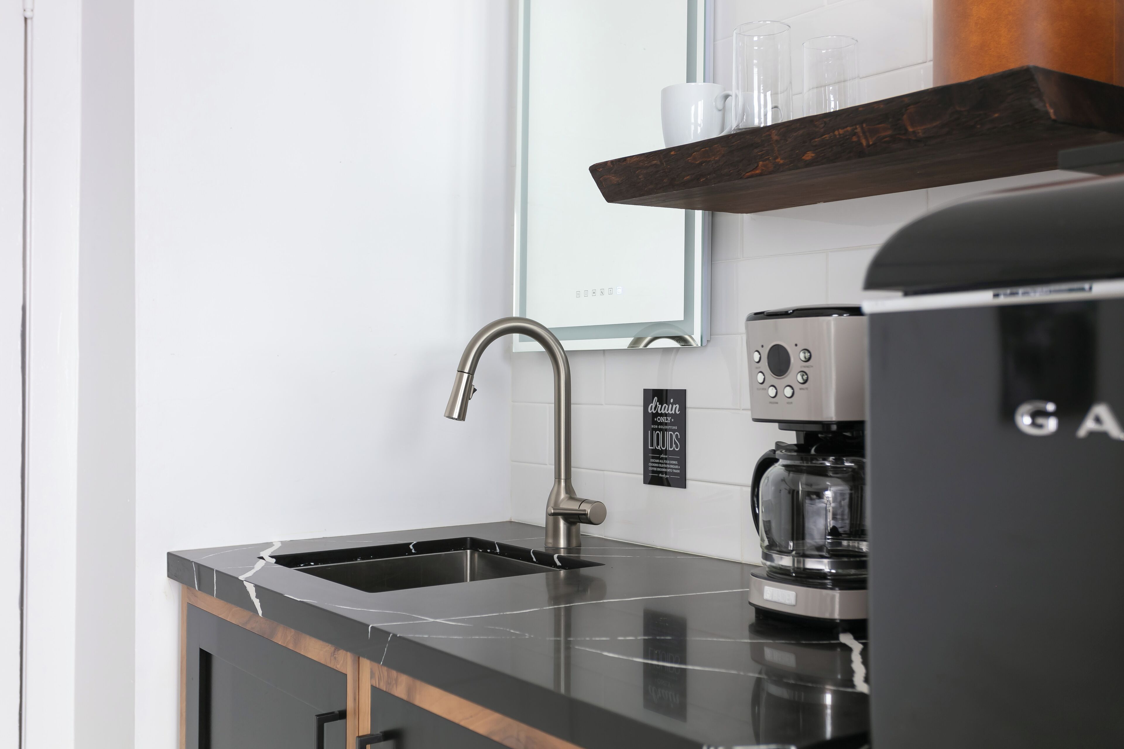 A modern kitchen with a black countertop, stainless steel faucet, and a coffee machine.