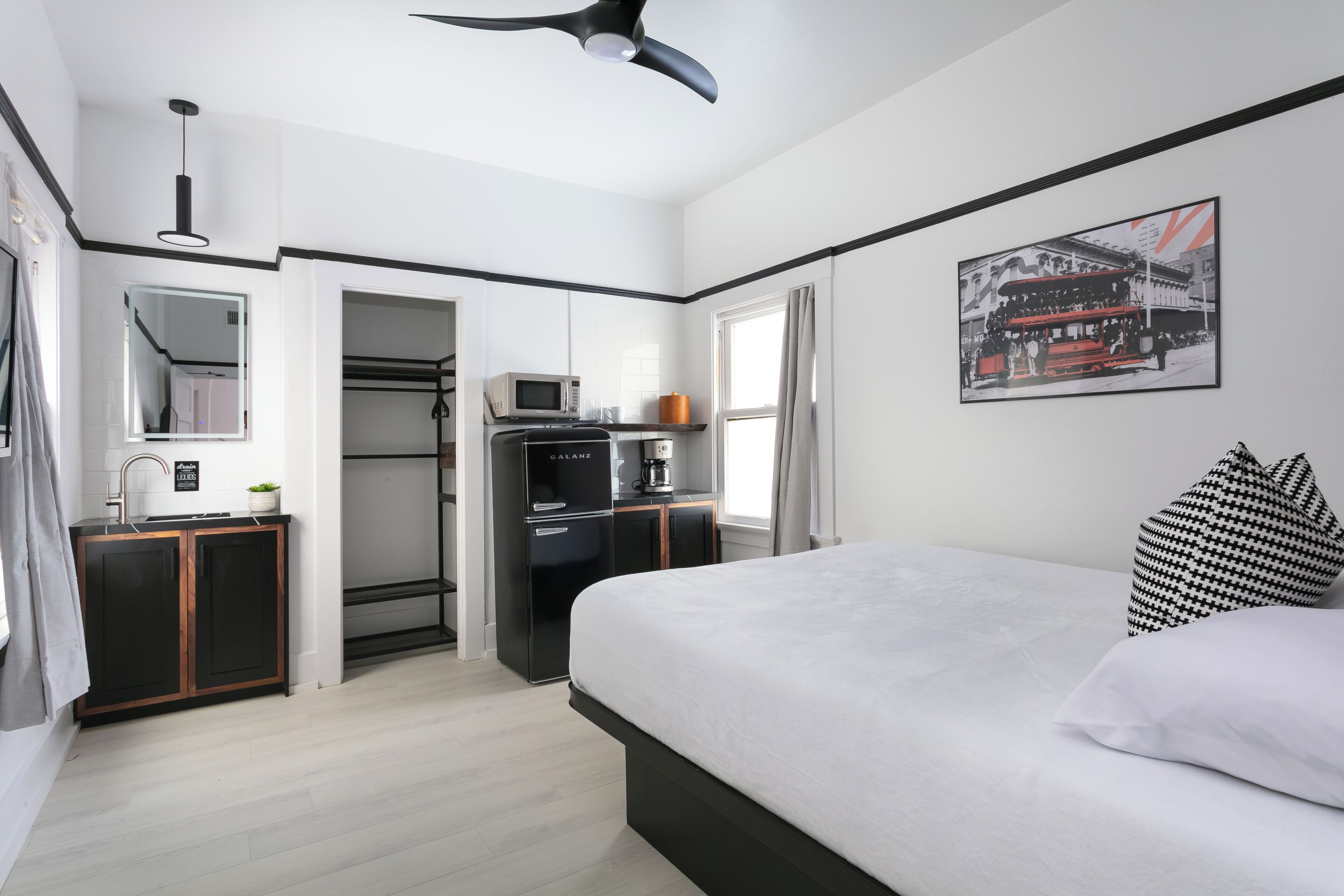 A modern hotel room with a bed, a kitchenette, a microwave, a coffee machine, and a framed picture on the wall.
