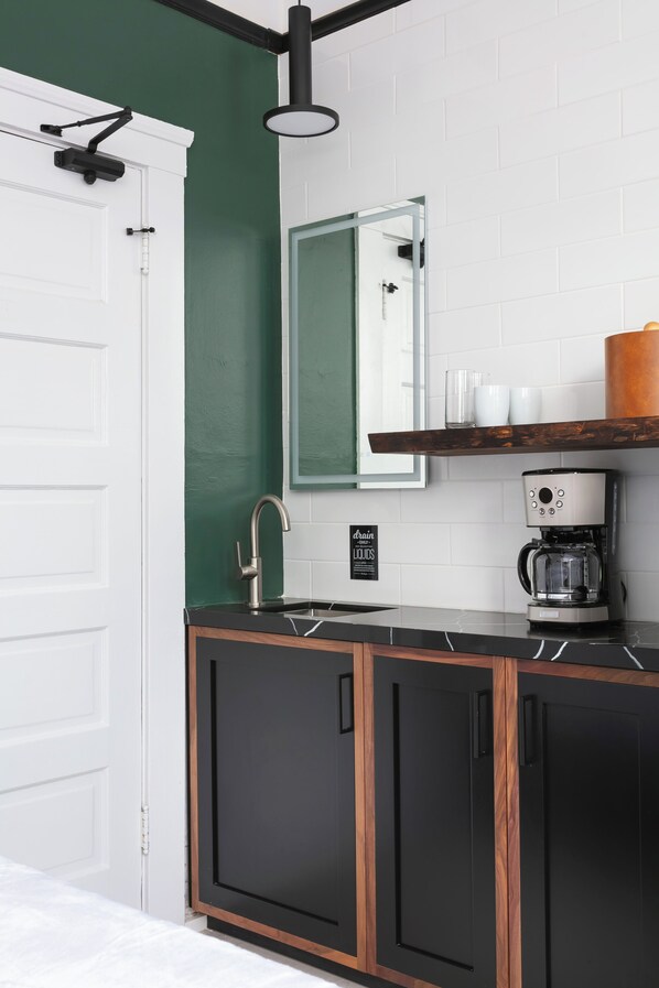 Una cocina moderna con una paleta de colores blanco y negro, una cafetera y una alacena con tazas.