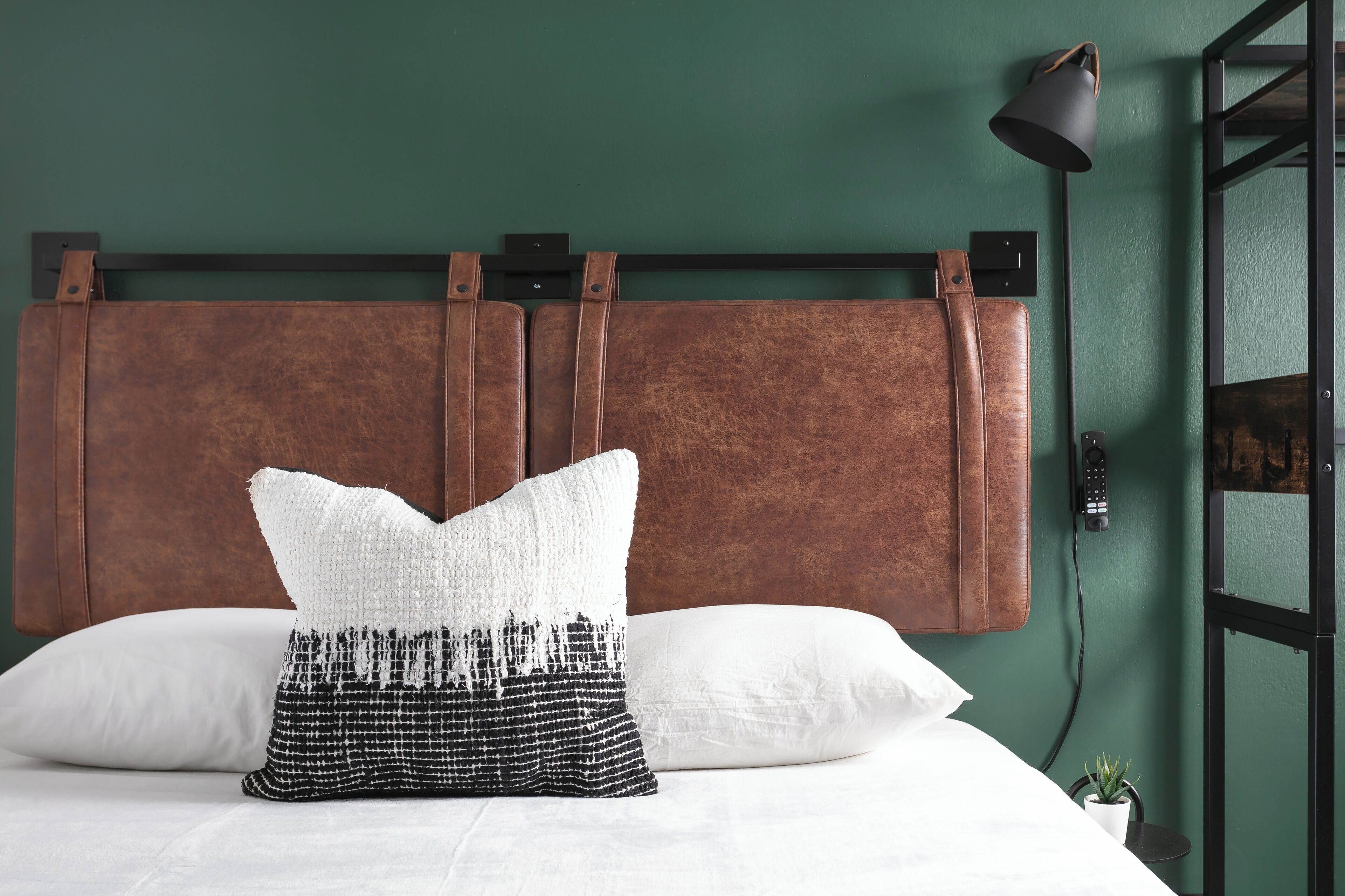 A bed with white and black patterned pillows, a brown headboard, and a small potted plant on the side.