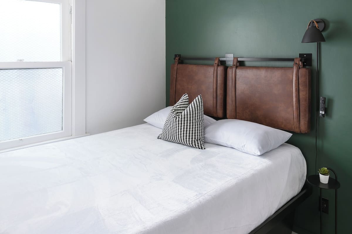A bedroom with a bed, a ceiling fan, a window, and a nightstand with a lamp.