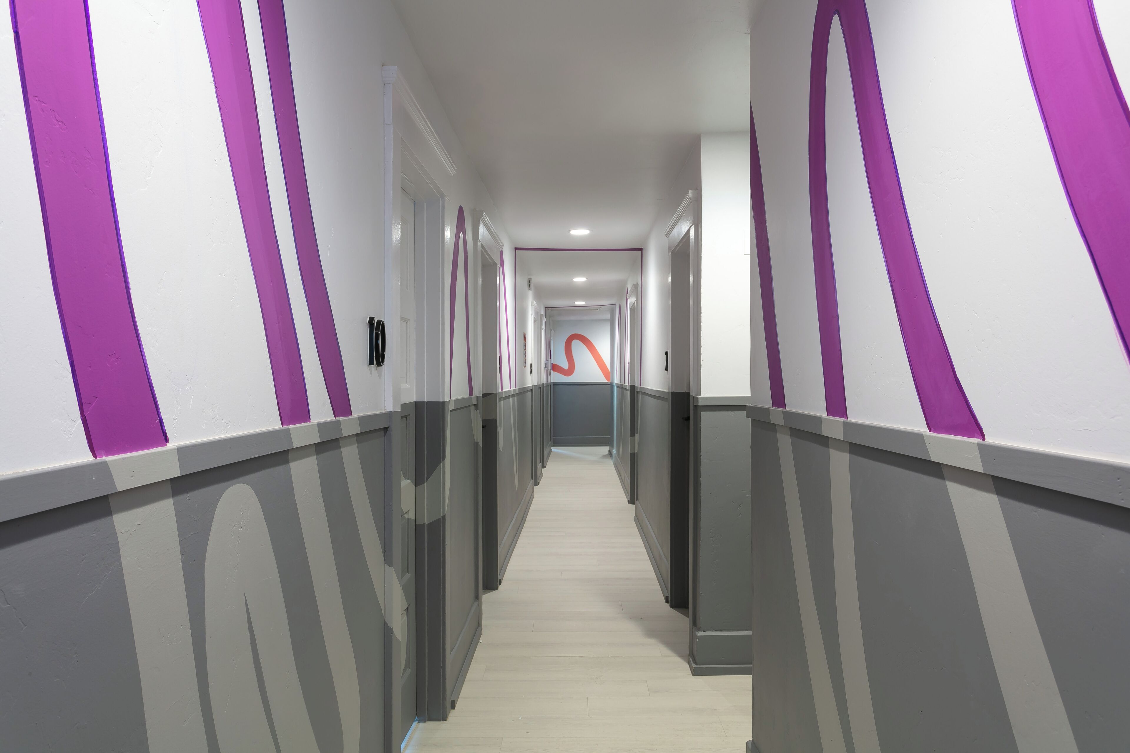 A hallway with alternating white and purple walls, a light-colored floor, and a modern design.