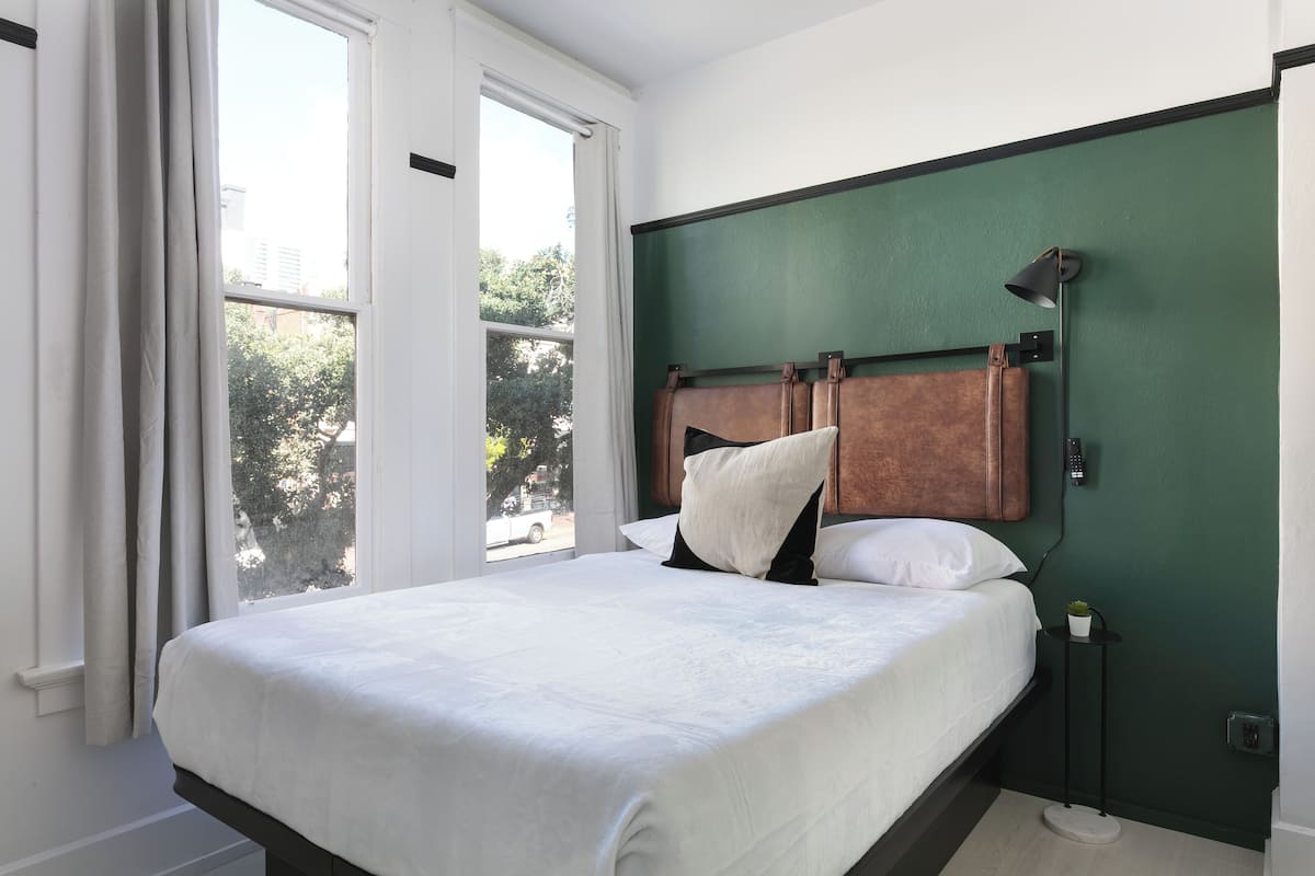 A bedroom with a large bed, a nightstand, a lamp, and a view of the outdoors.