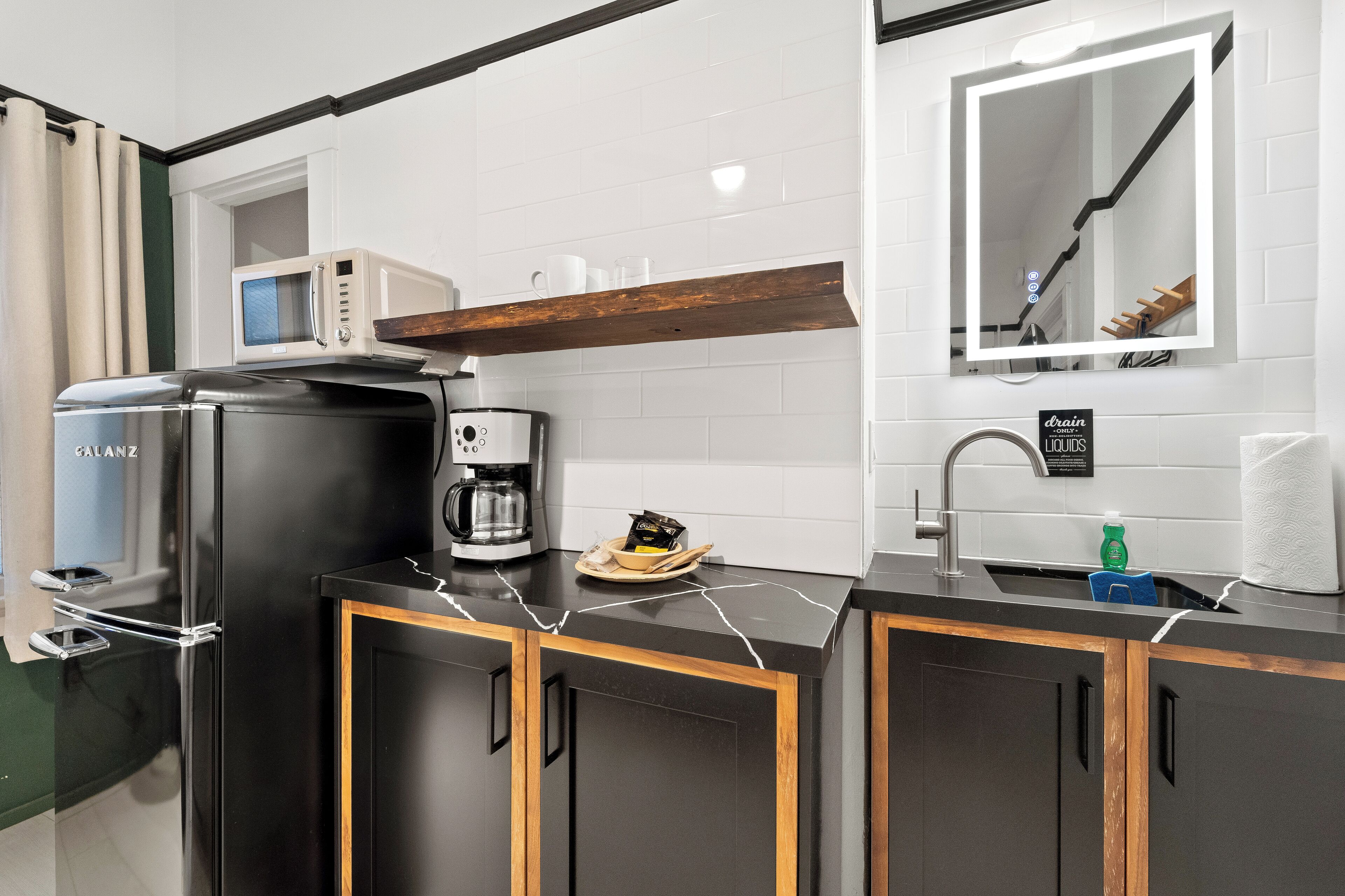 Una cocina moderna con un refrigerador negro, cafetera y microondas.