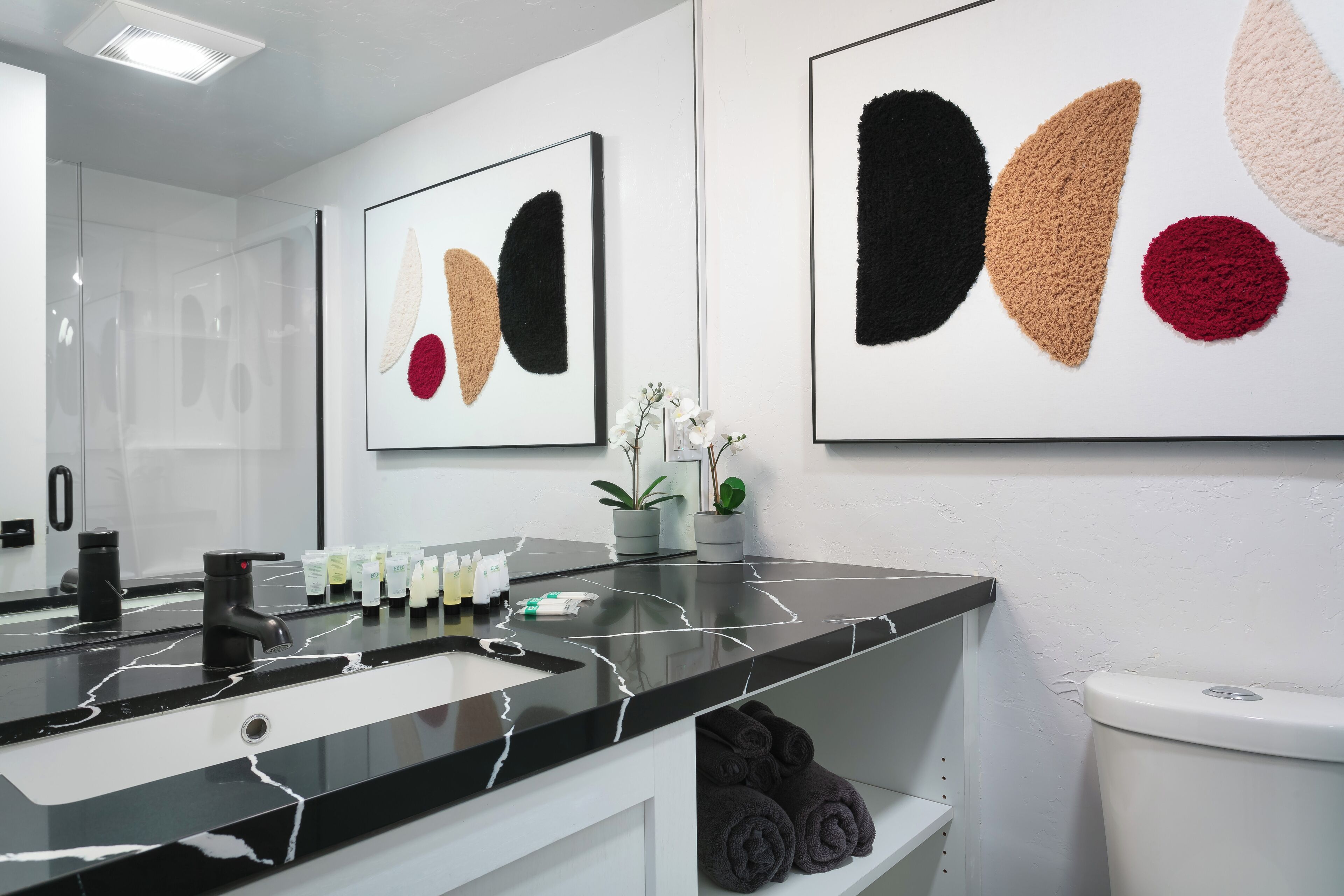 Ein modernes Badezimmer mit einem schwarzen Marmorwaschbecken, einer Toilette und abstrakter Kunst an den Wänden.