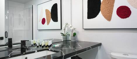 Ein modernes Badezimmer mit einem schwarzen Marmorwaschbecken, einer Toilette und abstrakter Kunst an den Wänden.