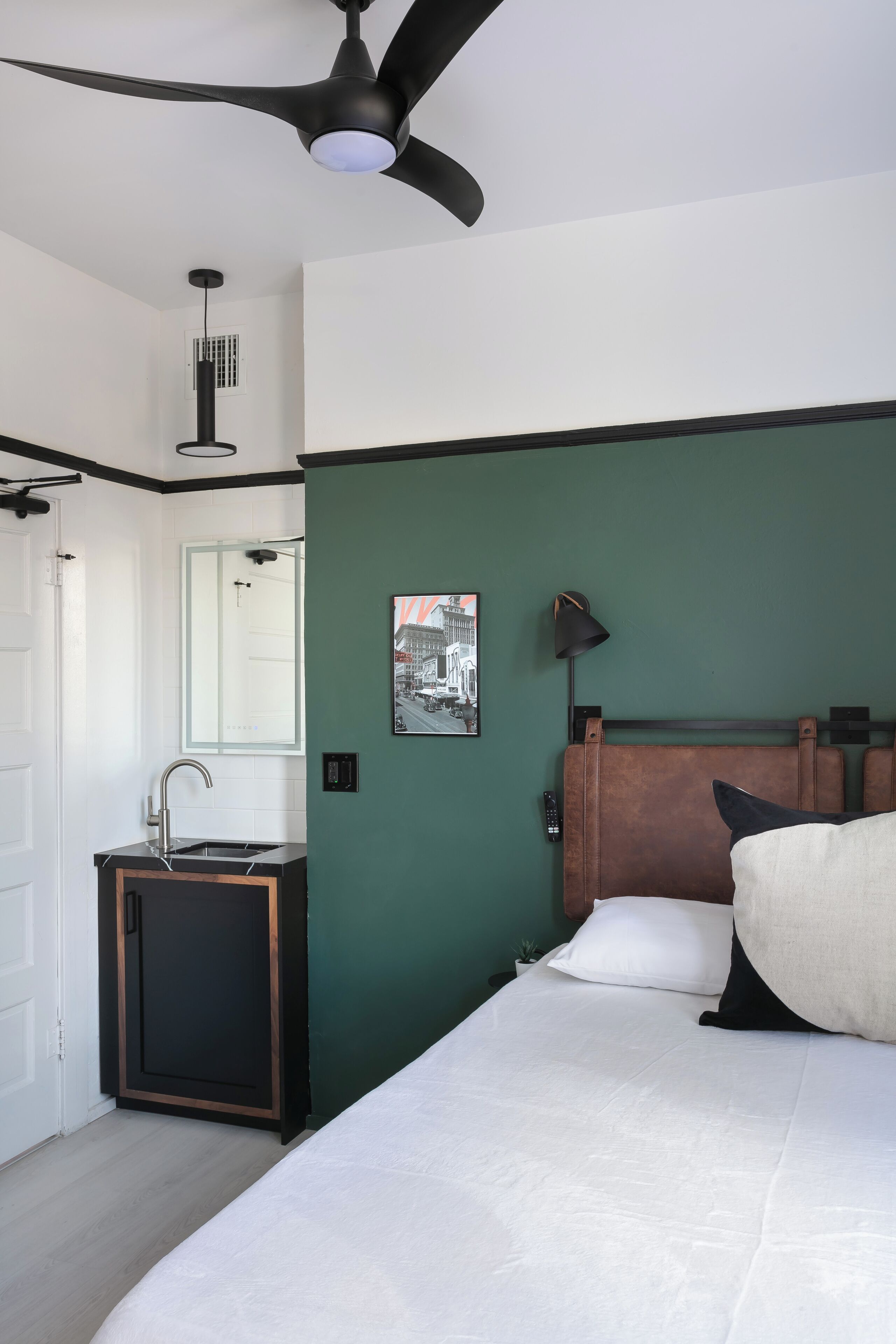Een slaapkamer met een bed, nachtkastje, plafondventilator, raam en deur.