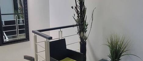 A modern living room with a black sofa, a small table, a potted plant, and a staircase leading to another level.