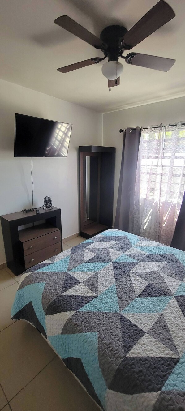 A bedroom with a bed, a ceiling fan, a TV, a dresser, and a window with curtains. - Casa Nueva Vista Al Mar 6p 3R 3B Mascota (Ensenada)
