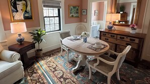 Ein Essbereich mit einem runden Tisch, Stühlen, einer Lampe, einem Blumentopf und einem Spiegel an der Wand.