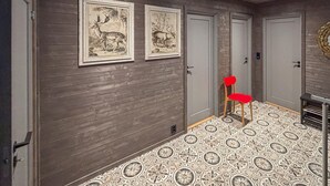 A hallway with wooden walls, two framed animal paintings, a red chair, and patterned floor tiles.