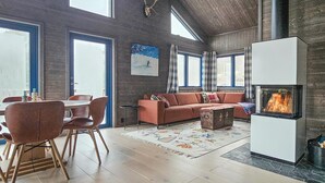 A spacious living room with a high ceiling, a fireplace, a large window, and a cozy seating area.