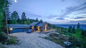 A cabin with a gravel driveway, a car parked in front, and a view of the ocean.