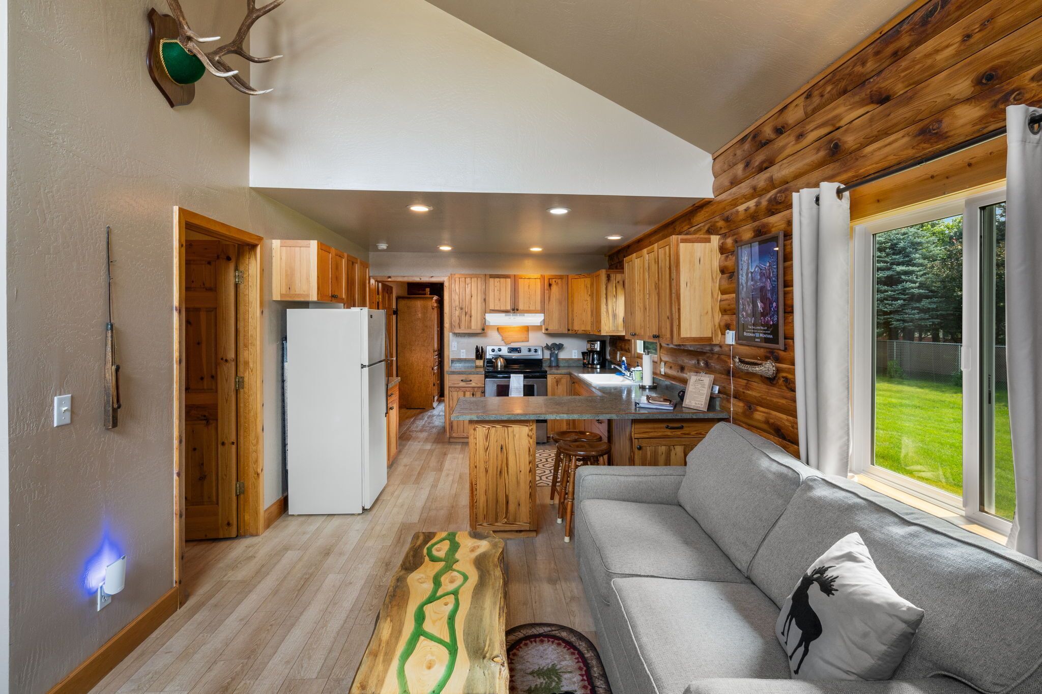 A modern kitchen with wooden cabinets, a central island, and a large window overlooking a green landscape.