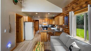 A modern kitchen with wooden cabinets, a central island, and a large window overlooking a green landscape.