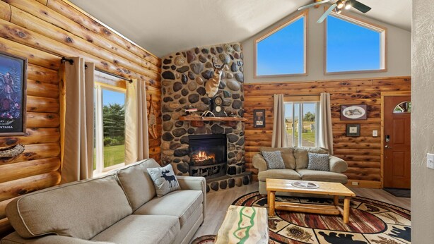 L'intérieur d'une cabane en rondins, avec une cheminée en pierre, un canapé, une table basse et une vue sur l'extérieur.