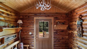 L’intérieur d’un chalet en bois, avec une porte portant l’inscription « SORTIE », un banc avec des coussins, une lampe et une décoration représentant une tête de cerf.