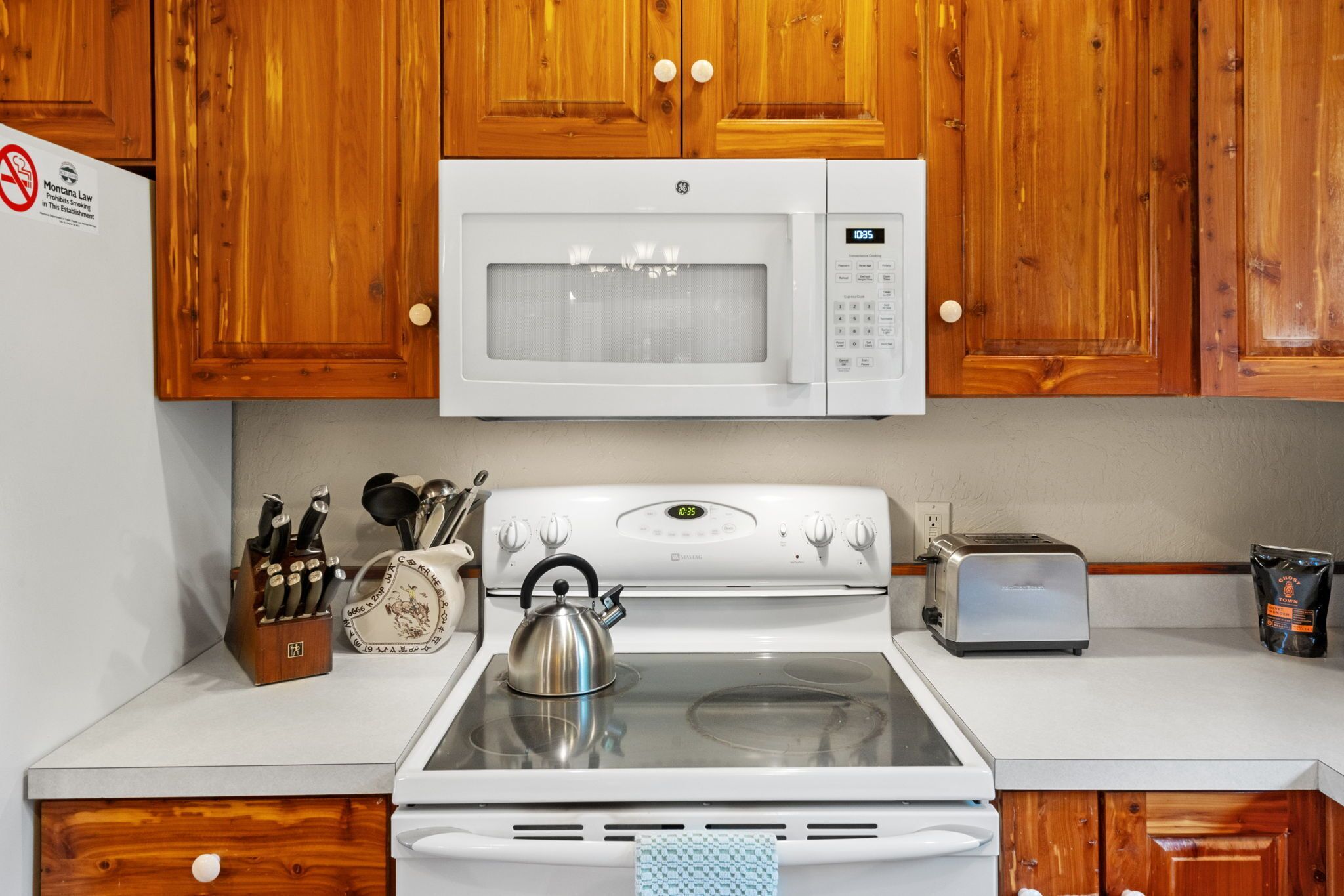 A kitchen with wooden cabinets, a microwave, a stove, a toaster, and a kettle.
