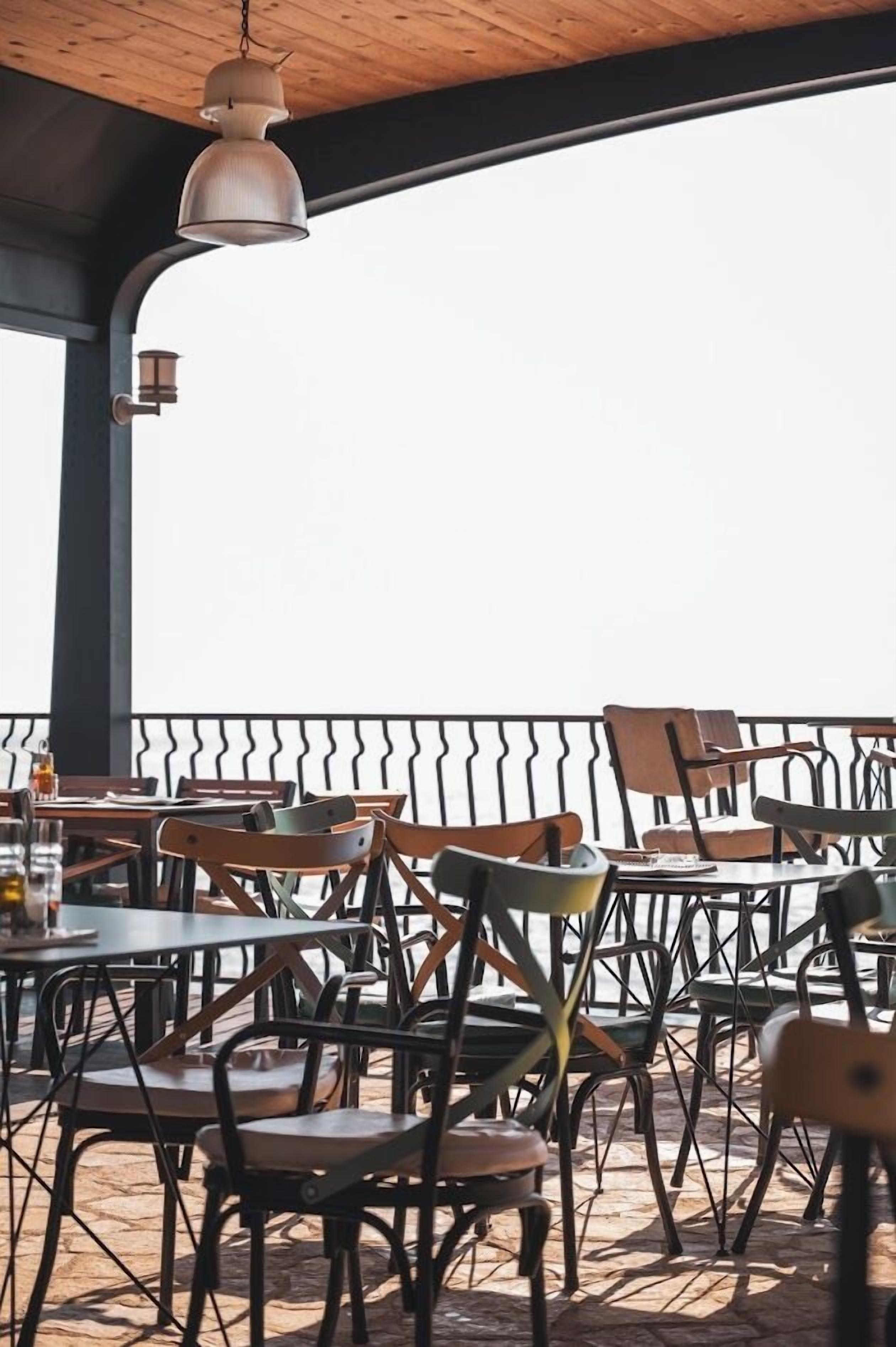 An outdoor seating area with tables and chairs, a hanging light fixture, and a view of the sea.