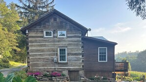 A rustic log cabin with a stone foundation, a wooden deck, and a well-maintained lawn. - Cozy, scenic, studio apartment for nature-lovers ! (Paris)