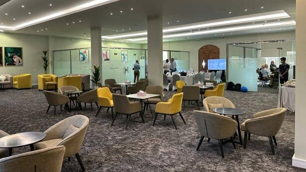 A spacious lobby with multiple seating areas, including yellow and beige chairs, and tables. There are glass partitions and a large screen displaying information. - hotel alfal alshemaly (Duba)