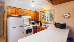 Una cocina con armarios de madera, un refrigerador blanco, estufa, microondas y ventana con vista a árboles.