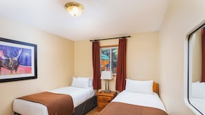 Habitación de hotel con dos camas individuales, una mesita de noche con lámpara, un cuadro enmarcado en la pared y una ventana con cortinas.