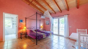 Un dormitorio con cama con dosel, dos lámparas de noche, una ventana con vistas y una silla blanca.