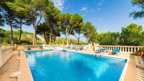 Una piscina azul cristalina con sillones de descanso y barandilla, rodeada de árboles y un cielo despejado.