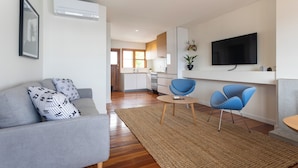 A modern living room with a grey sofa, two blue chairs, a small round table, and a TV mounted on the wall. - 2-bed apartment in the heart of Ponsonby (Auckland)