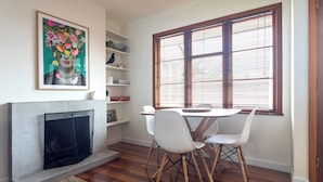 A dining area with a fireplace, white chairs, a table, and a window with blinds. - 2-bed apartment in the heart of Ponsonby (Auckland)