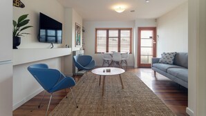 A modern living room with a flat-screen TV, blue chairs, a round coffee table, and a grey sofa. - 2-bed apartment in the heart of Ponsonby (Auckland)