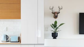 A modern kitchen with white cabinets, a wooden upper shelf, a blue chair, a potted plant, and a mounted deer head. - 2-bed apartment in the heart of Ponsonby (Auckland)