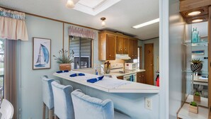 A modern kitchen with a central island, bar stools, wooden cabinets, and a large window with a sailboat painting.