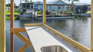 A wooden deck with a built-in sink, overlooking a calm water body with houses in the background.