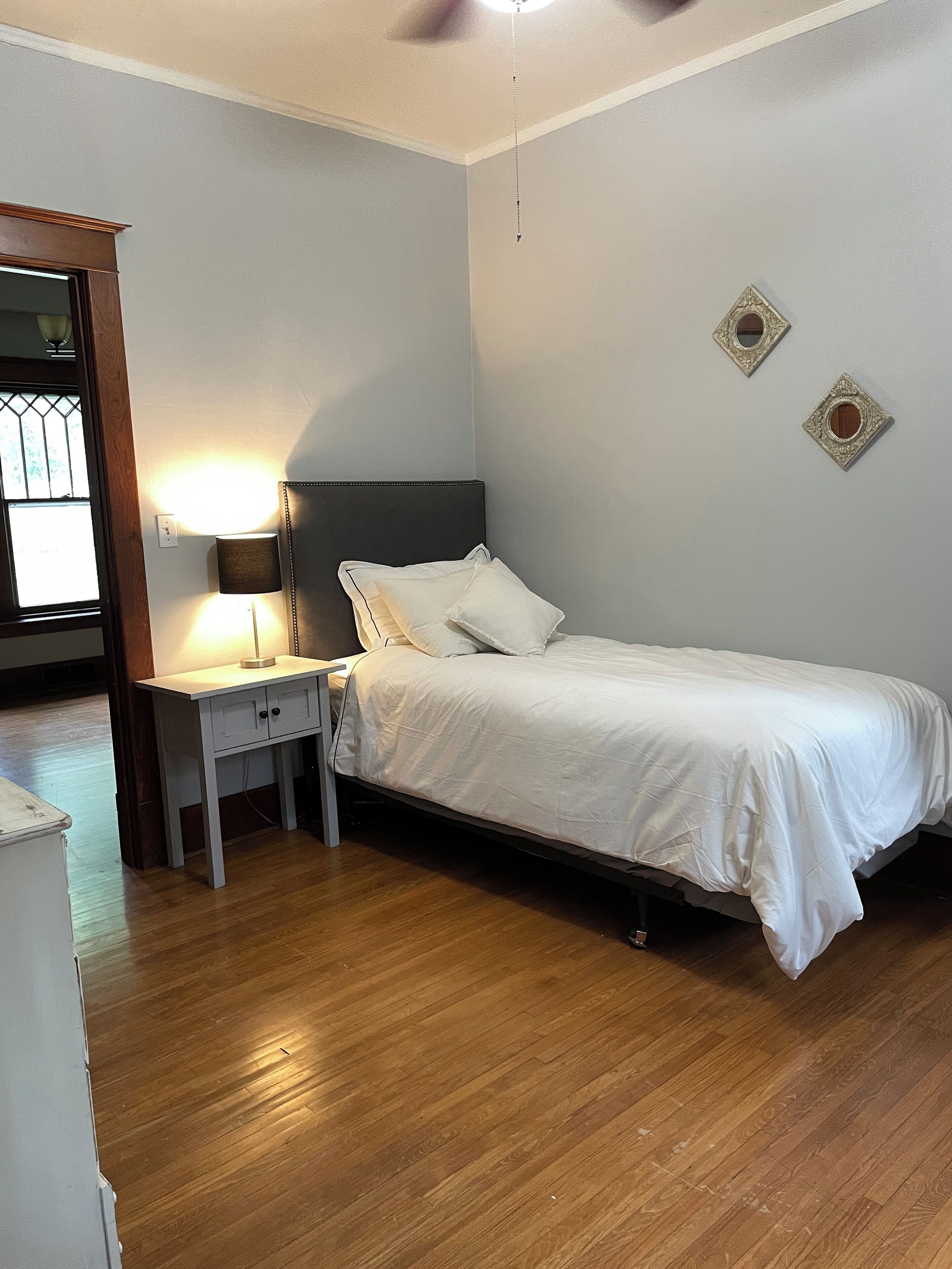 A bedroom with a single bed, a nightstand, a lamp, and a small desk.