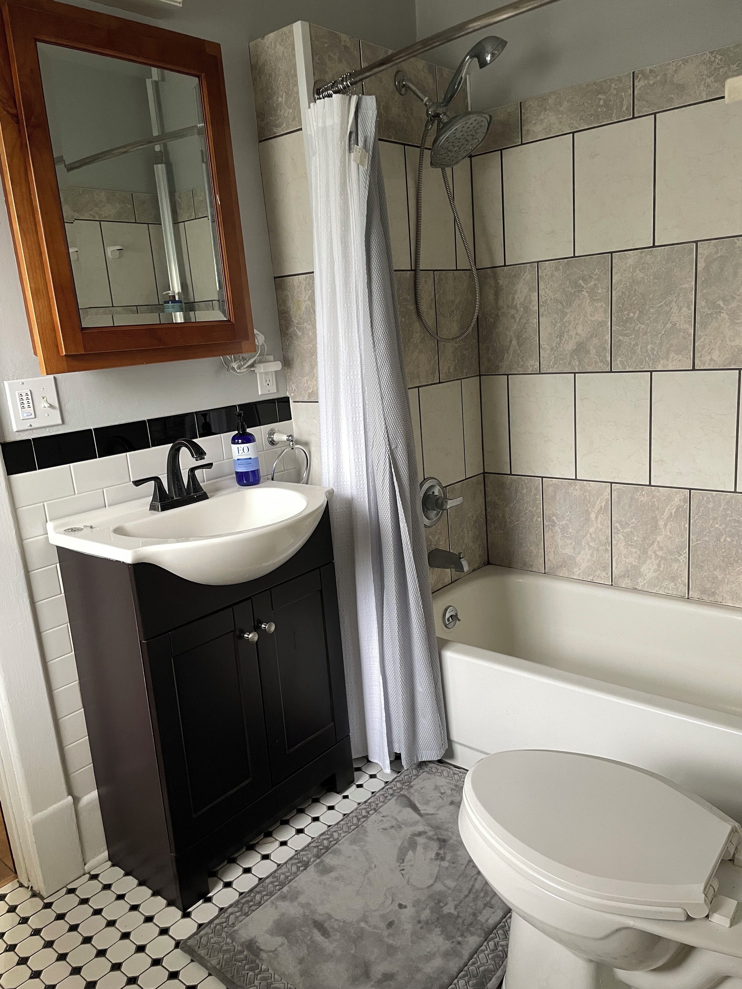 Een badkamer met een wit wastafelmeubel, zwarte kasten, een wit toilet en een bad.