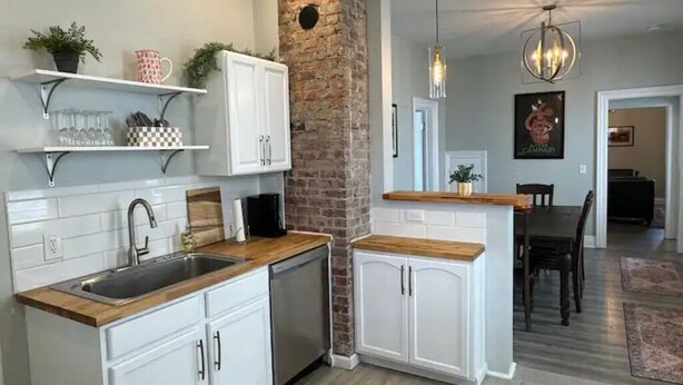 A modern kitchen with white cabinetry, a brick accent wall, and a wooden countertop. - Reno'd 5Pts Buffalo Gem - Parking/Walkable with WiFi and AC (Buffalo)