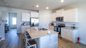 A modern kitchen with white cabinets, granite countertops, stainless steel appliances, and a central island with bar stools. - Enjoy a spacious 5-bedroom house all to yourself with easy beach access or Pools (Port Saint Joe)