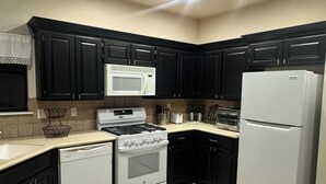Une cuisine avec des meubles de couleur sombre, une cuisinière blanche, un four à micro-ondes blanc et un réfrigérateur blanc.