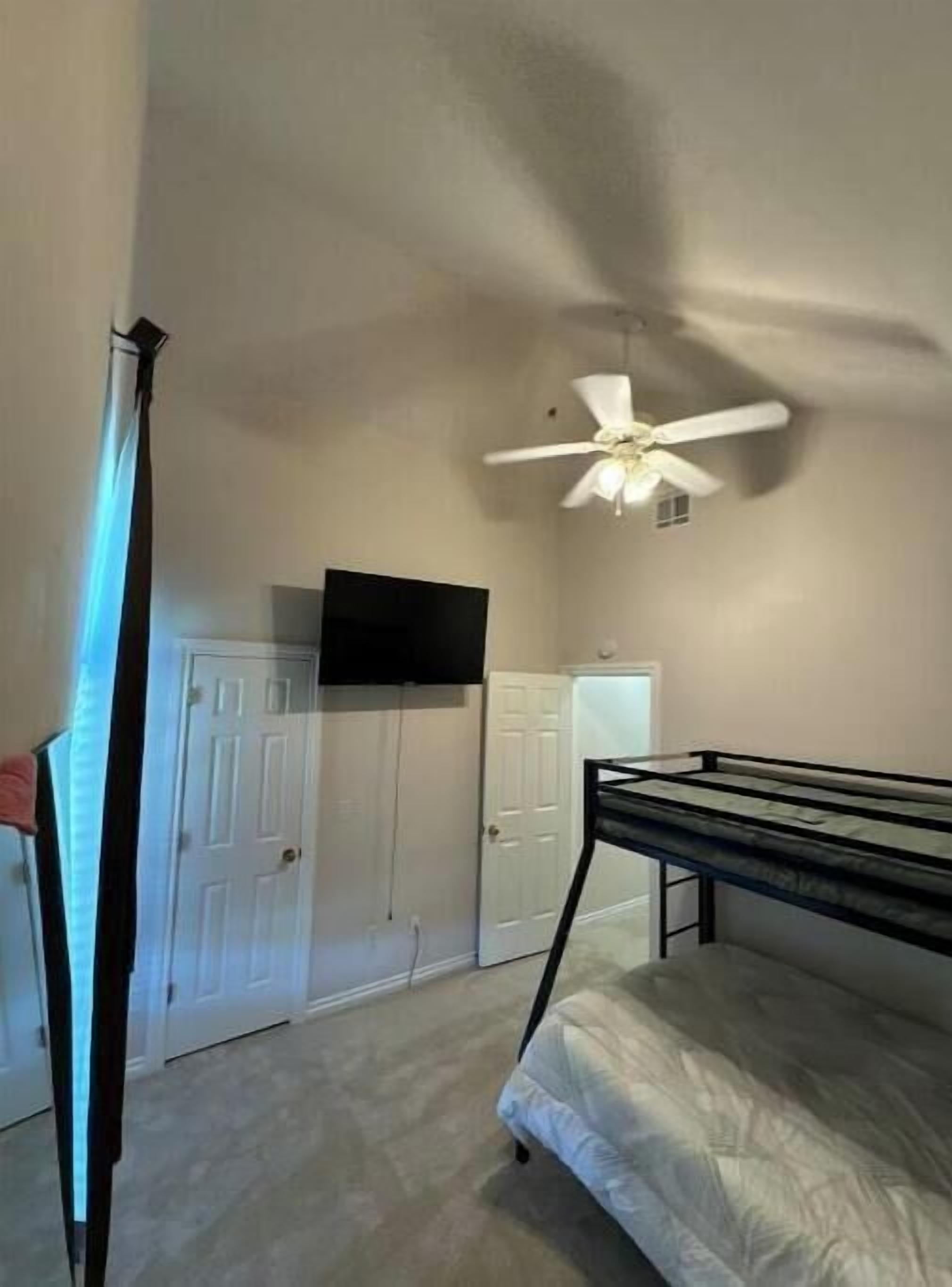 A bedroom with a bunk bed, a ceiling fan, a TV mounted on the wall, and a wardrobe.