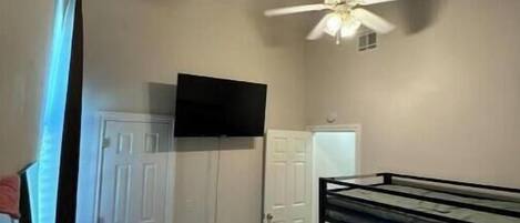 A bedroom with a bunk bed, a ceiling fan, a TV mounted on the wall, and a wardrobe.